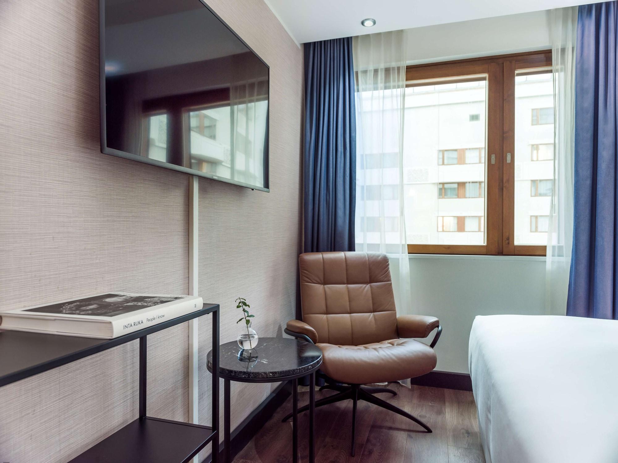 Radisson Blu Royal Viking Hotel, Stoccolma Esterno foto The photo shows a modern hotel room featuring a comfortable arrangement. There is a large flat-screen TV mounted on the wall. Below the TV, a sleek, minimalistic table holds a book and a small decorative plant. Next to the table is a stylish brown ch