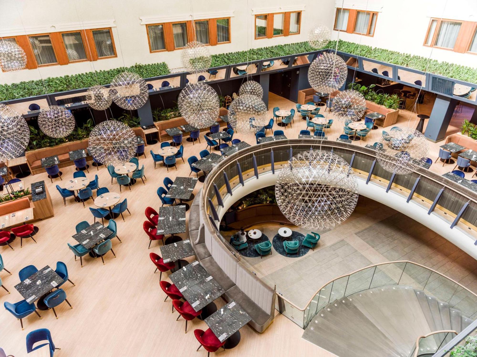 Radisson Blu Royal Viking Hotel, Stoccolma Esterno foto The photo shows a spacious and stylish dining area in a modern restaurant or hotel lobby. It features a variety of round tables arranged in a curved layout, surrounded by colorful chairs in shades of blue, red, and gray. Large, spherical light fixtur