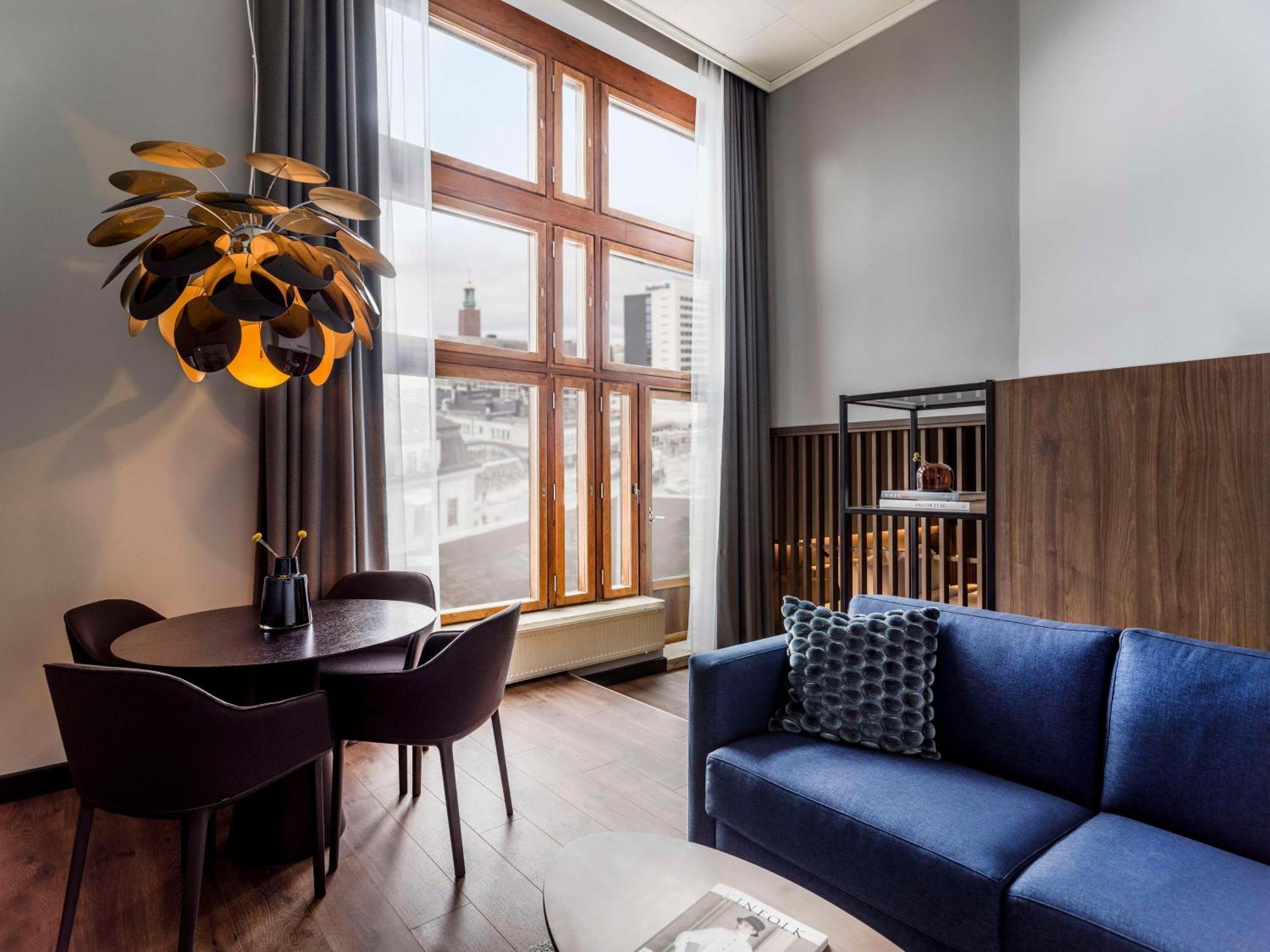 Radisson Blu Royal Viking Hotel, Stoccolma Esterno foto The photo shows a modern living space featuring a stylish interior design. There is a blue sofa positioned in the foreground, accompanied by a small round dining table and several chairs. The room is illuminated by a unique pendant light hanging from